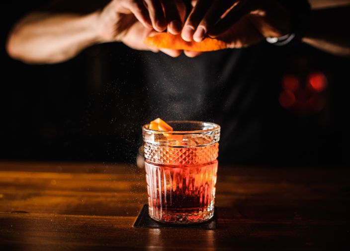 Bartender exprimiendo una piel de naranja sobre un cóctel Old Fashioned