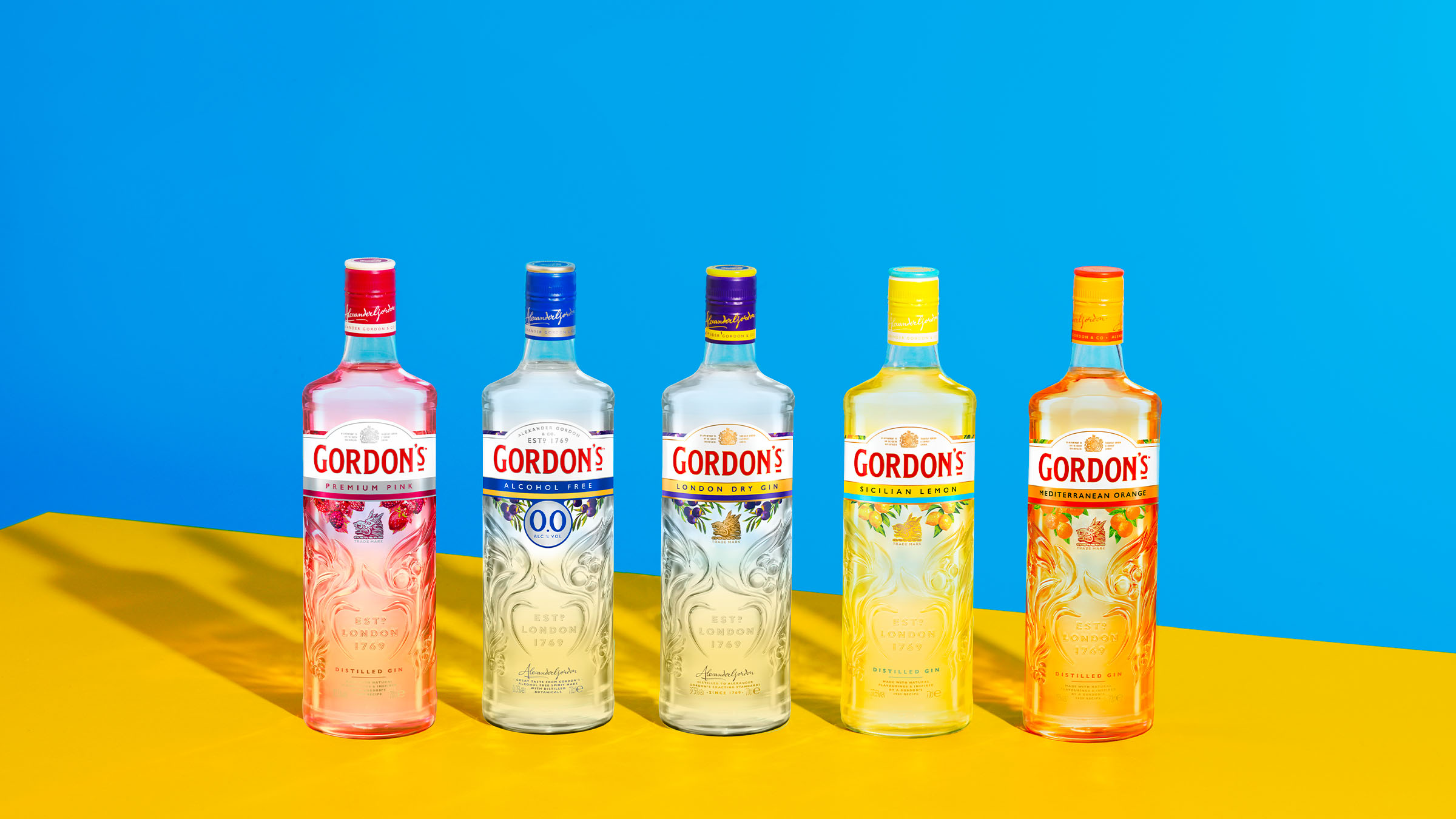 Five bottles of various Gordon’s gin variants on a bright blue and yellow background. 