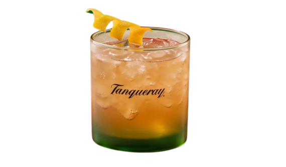 Copo baixo com base verde e logo preto da Tanqueray contendo um coquetel em tom âmbar com muito gelo. A borda é elegantemente decorada com uma casca de laranja em formato espiral. Fundo branco isolado.