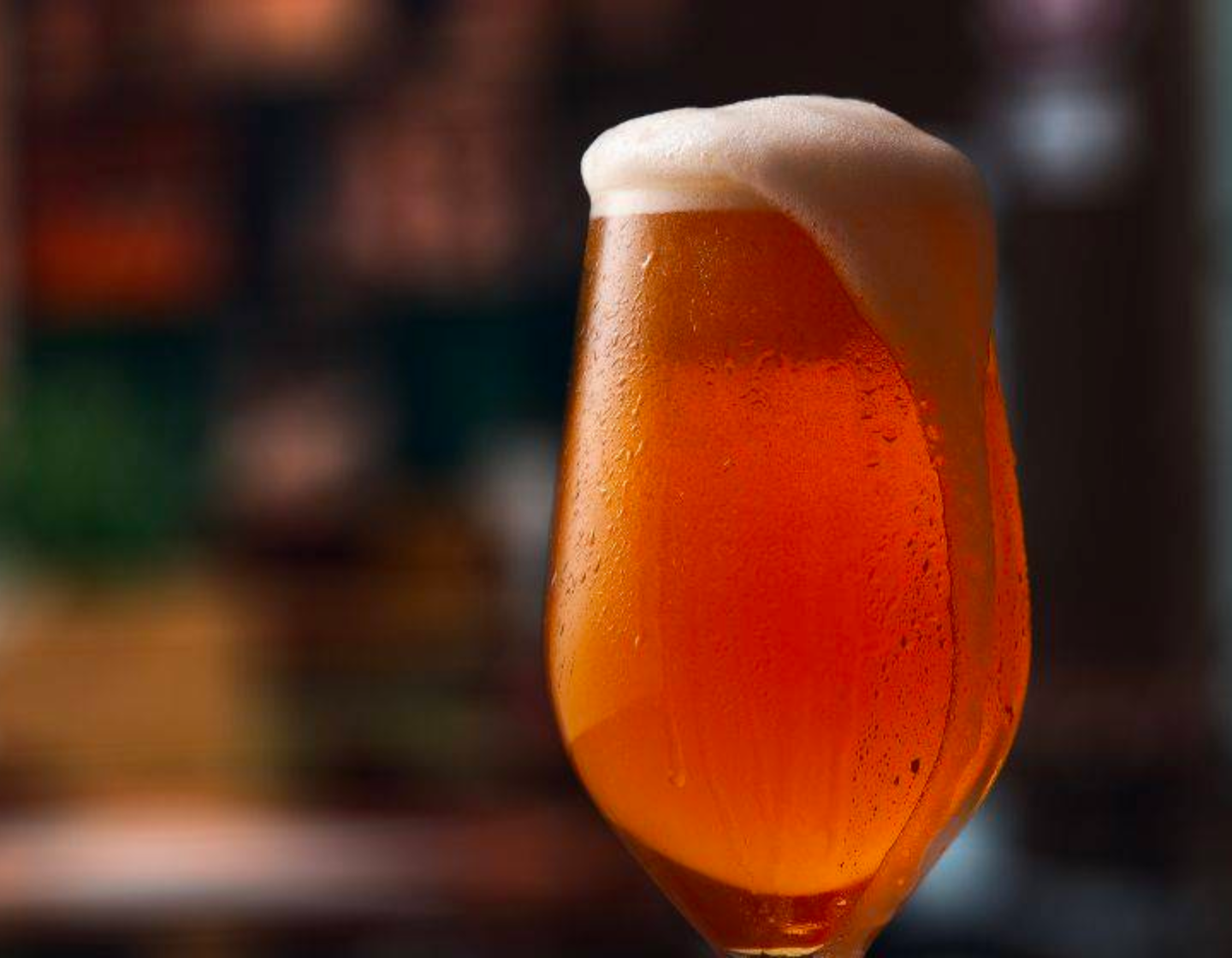 Pint of beer with foam spilling over the lip of the glass. 