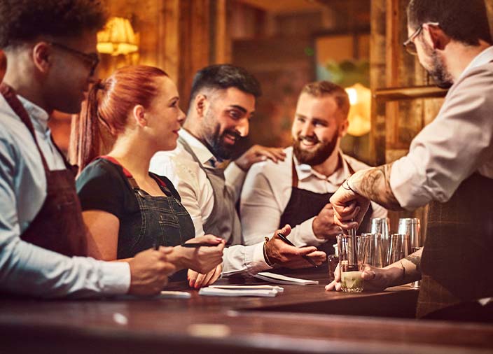A group of bar staff watching a cocktail be made together.  