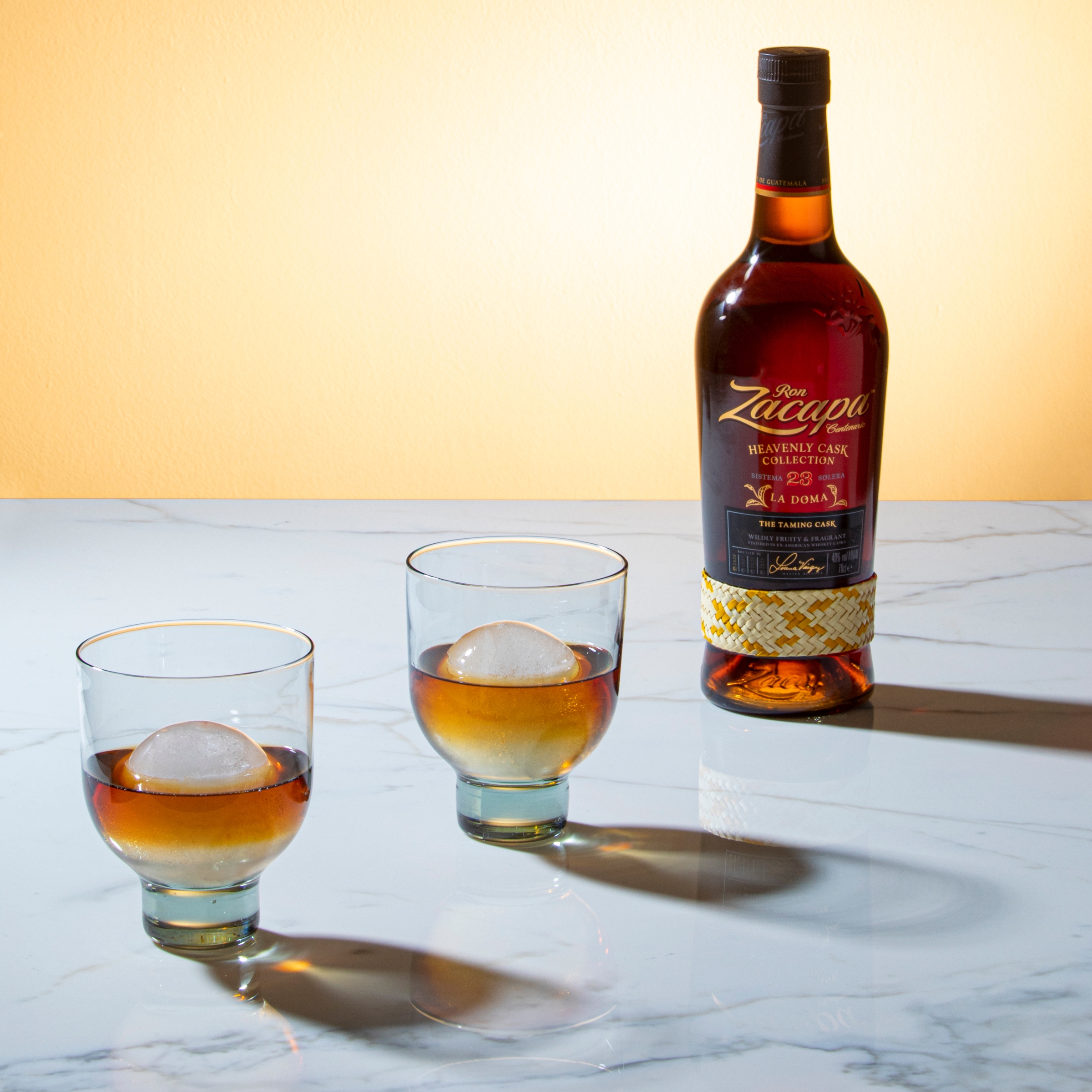Botella de Zacapa sobre una mesa junto a un cóctel y cerezas.