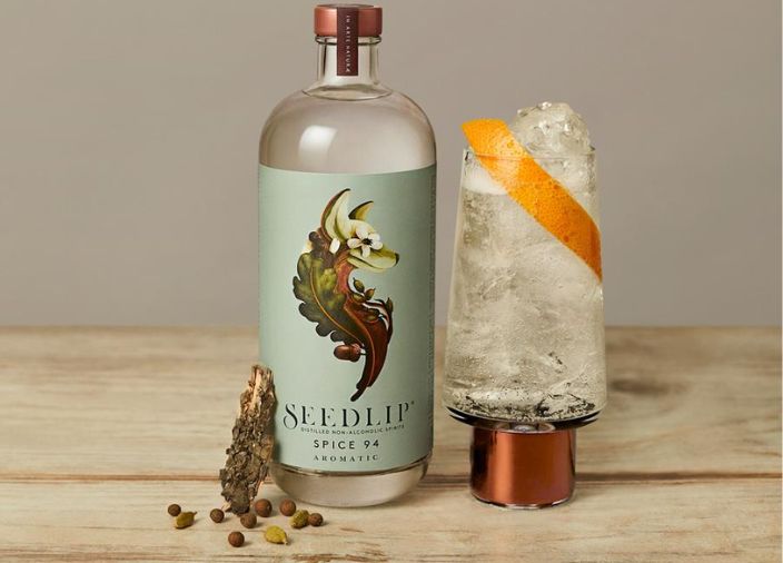 Bottle of Seedlip Spice 94 on table beside cocktail
