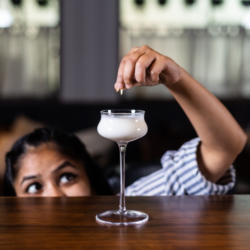 Uma mulher espreitando por baixo de uma mesa de madeira, decorando um coquetel de martini branco.