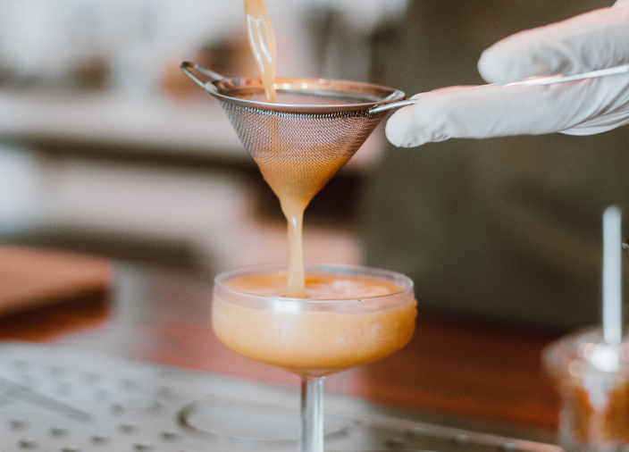 Eine Hand gießt einen Cocktail durch ein Sieb.
