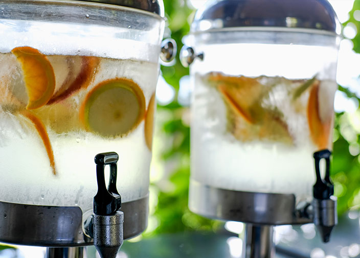 two cold drinks dispensers with taps filled with cocktail and fruit garnsih