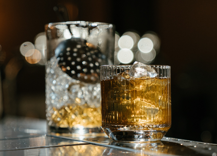 Ein Mixglas mit einem Sieb neben einem Cocktail.