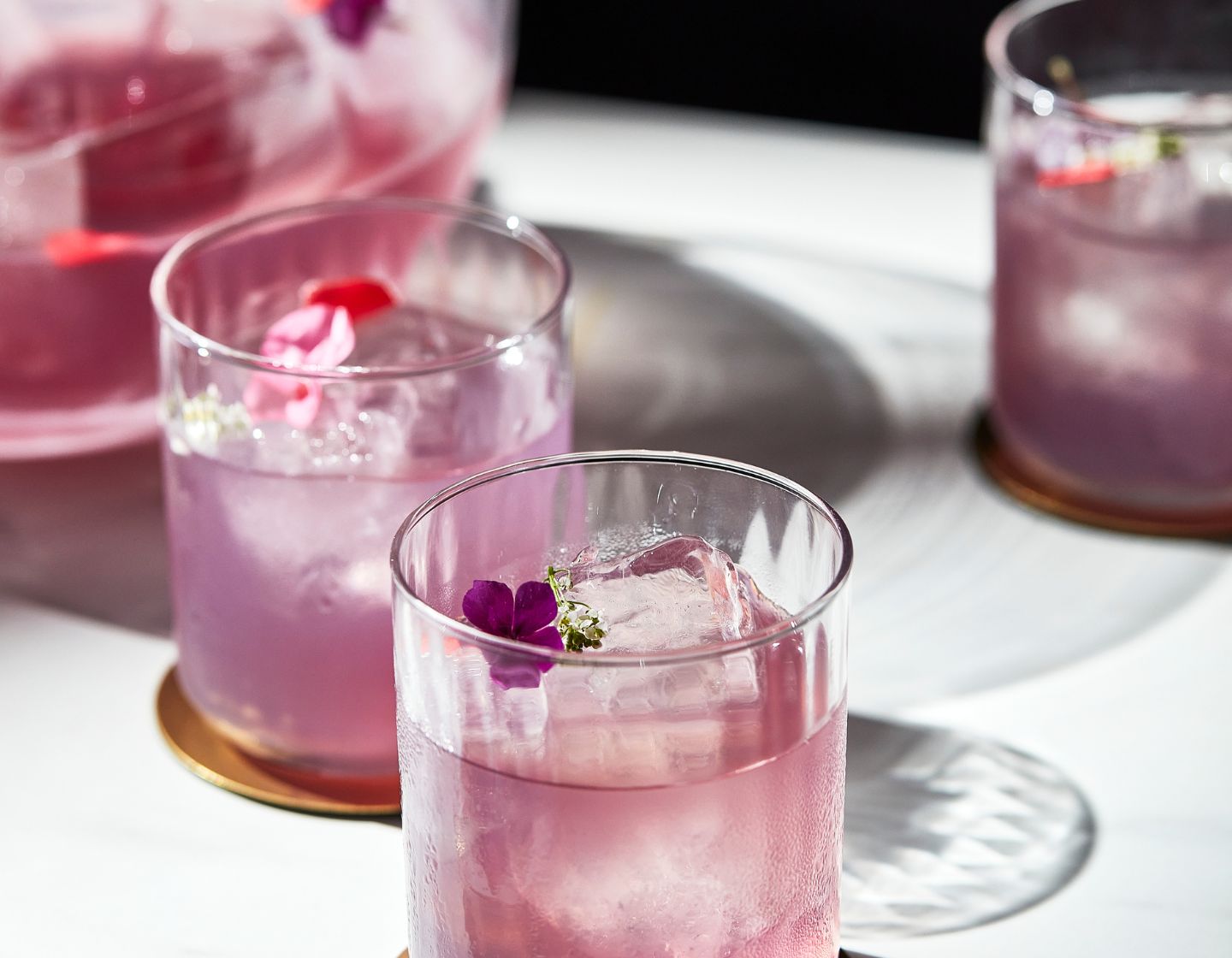 Cóctel morado servido con garnish de flores.