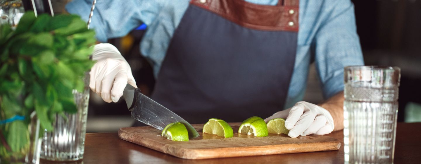 Imagem de um bartender cortando limões usando luvas em uma bancada 