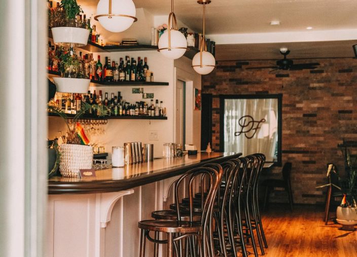 Bar setting with wooden stools and shelves with bottles.