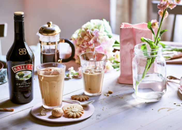 Botella de Baileys junto a dos vasos y un plato de galletas