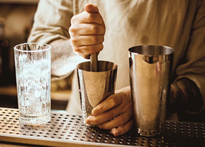 Barkeeper muddelt neben einem Glas mit Eis
