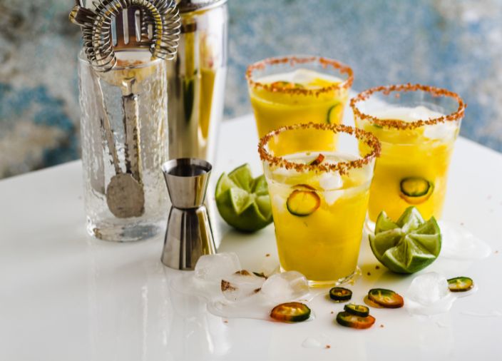 Tres cócteles picantes con utensilios de bar sobre la mesa