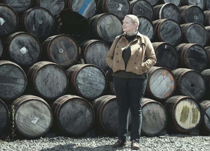 A person standing in front of stacked barrels.