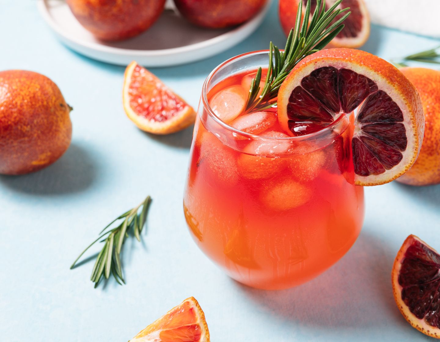 An orange coloured cocktail with citrus and herb garnish.