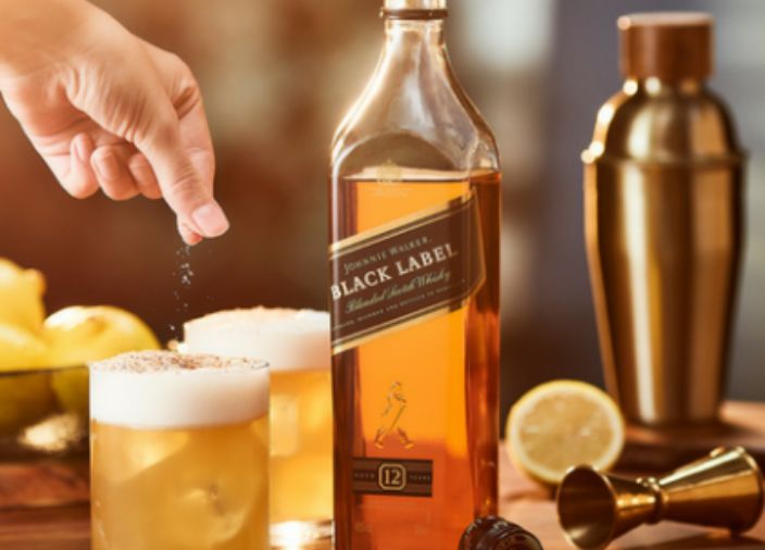 Whisky Sour junto a una botella de Johnnie Walker Black Label y limones.  