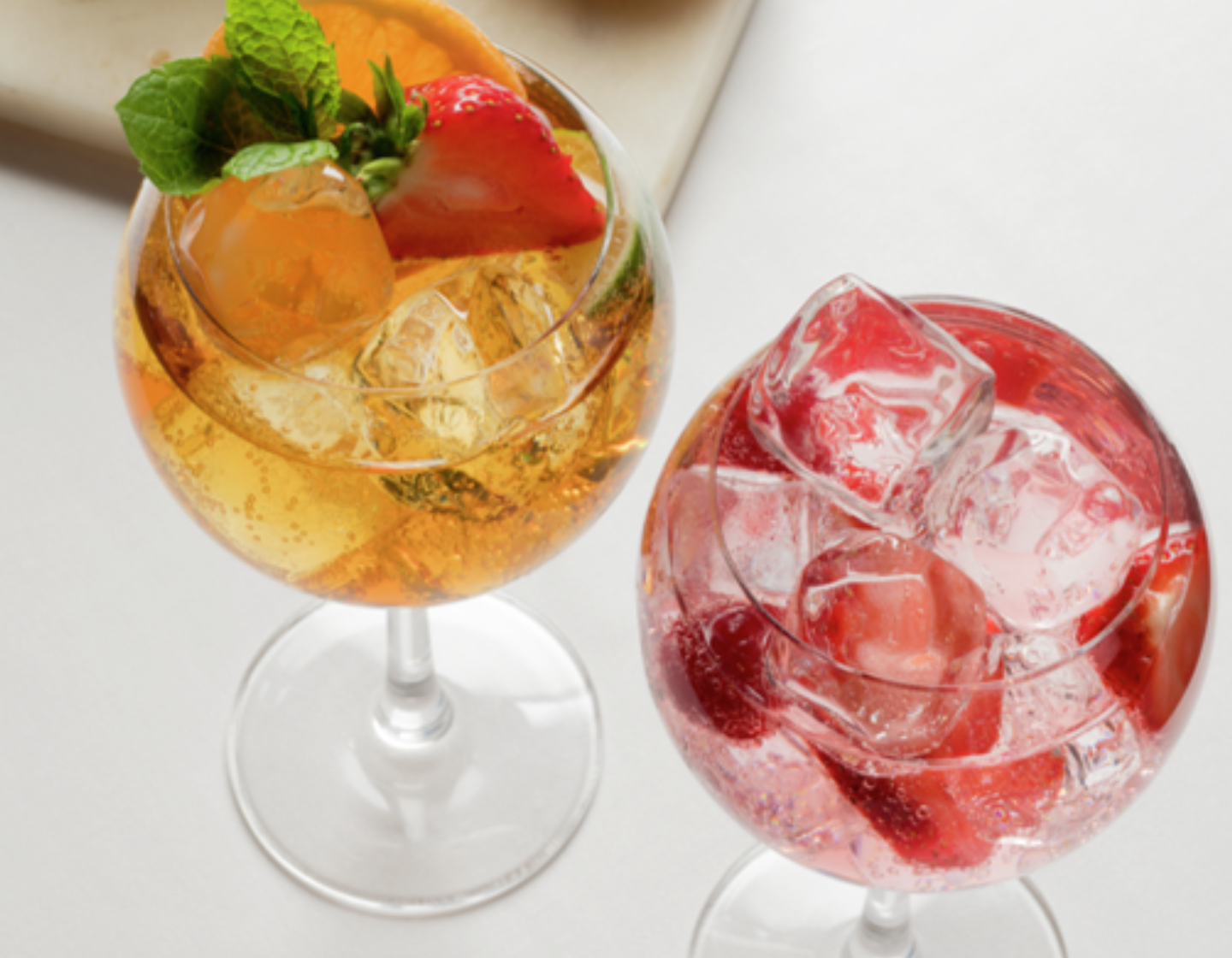 Dos coloridos cócteles en copas de ginebra con hielo y decoraciones de frutas