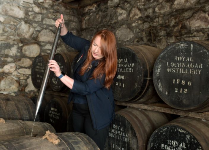 Mujer tomando muestra del barril de whisky
