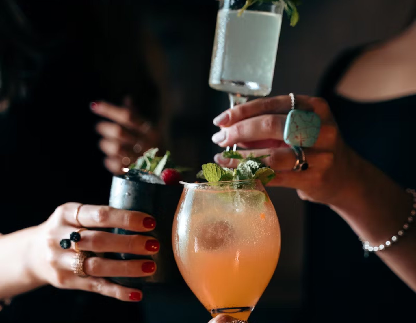 A selection of different gin-based cocktails staged together on a white table. Garnished with fruits and ice, next to a cocktail shaker.