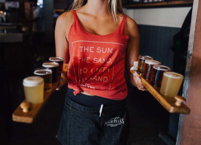 Female bartender carrying two trays of beers