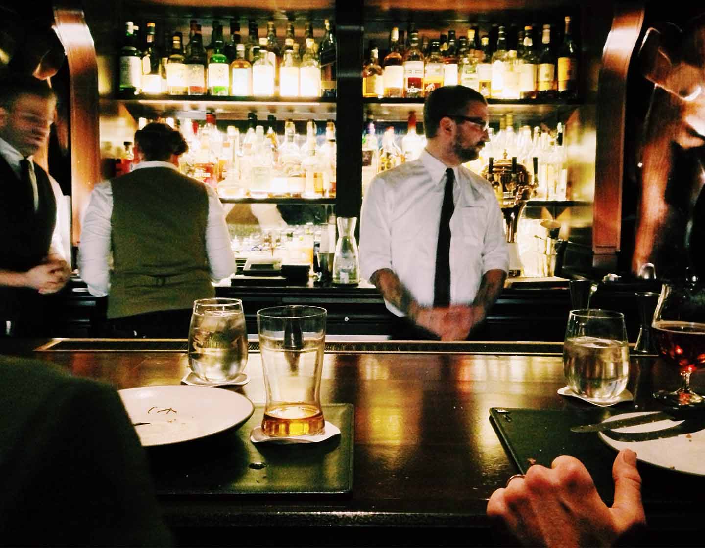 Equipe do bar trabalhando atrás de bar ocupada com clientes sentados no bar com comida e bebidas