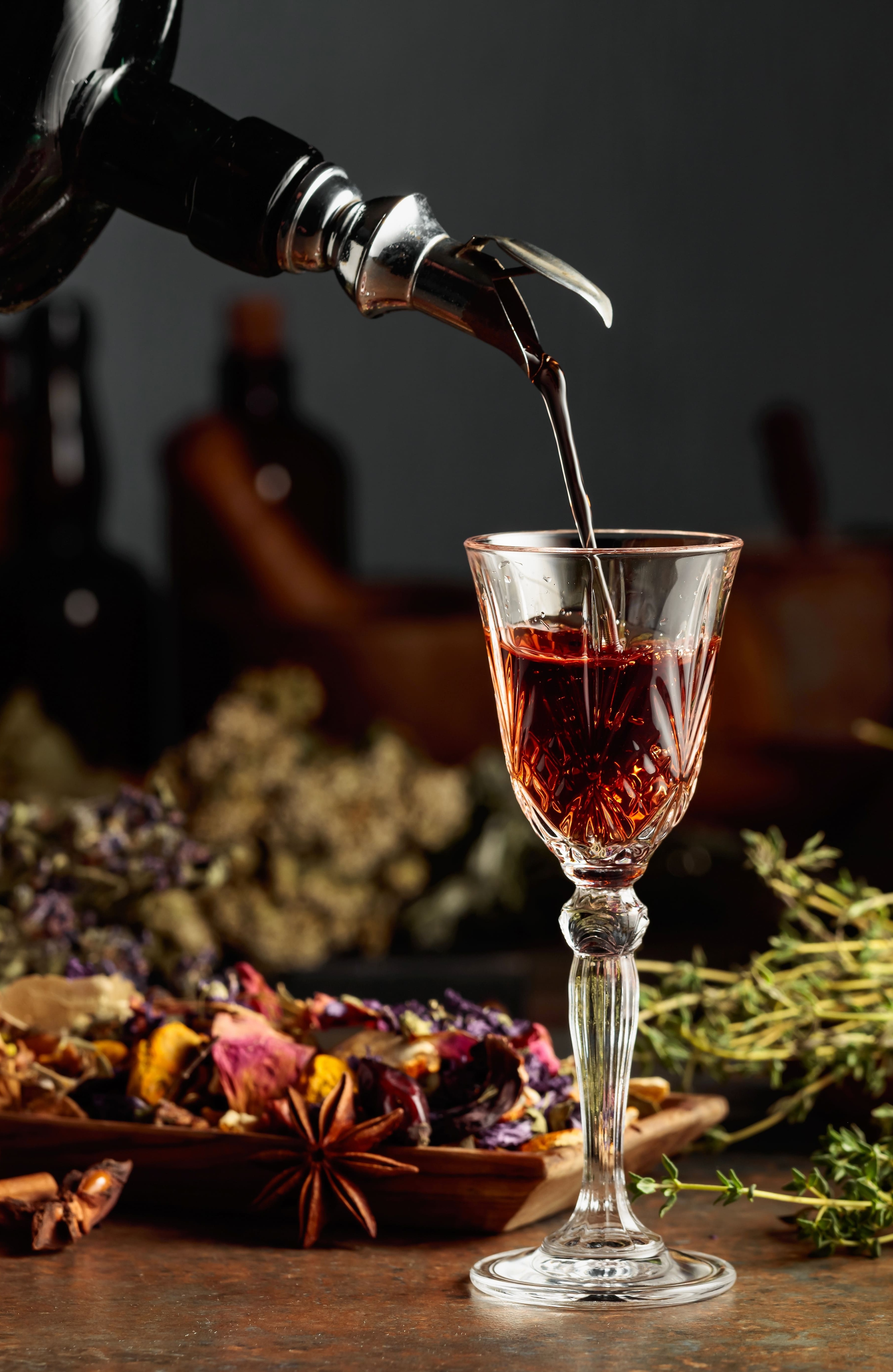 um cálice sobre uma mesa, com licor sendo servido nele. na mesa há diversas matérias primas de licores