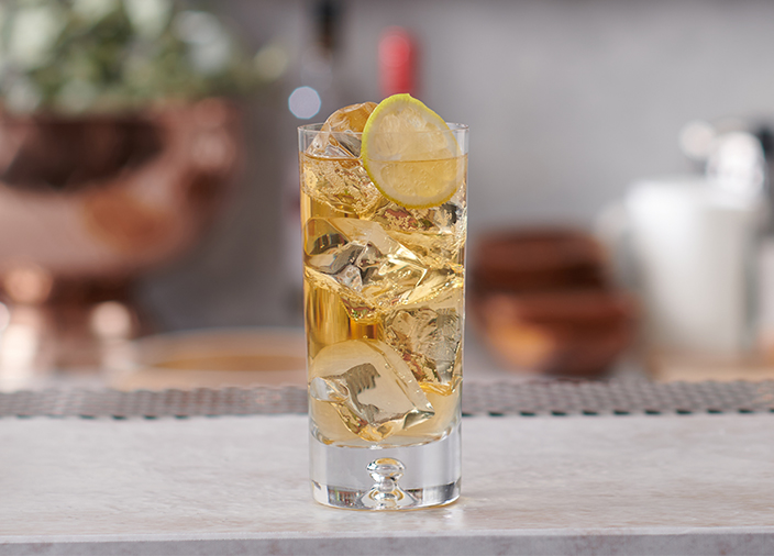 A tall highball glass filled with ice and amber coloured liquid. 