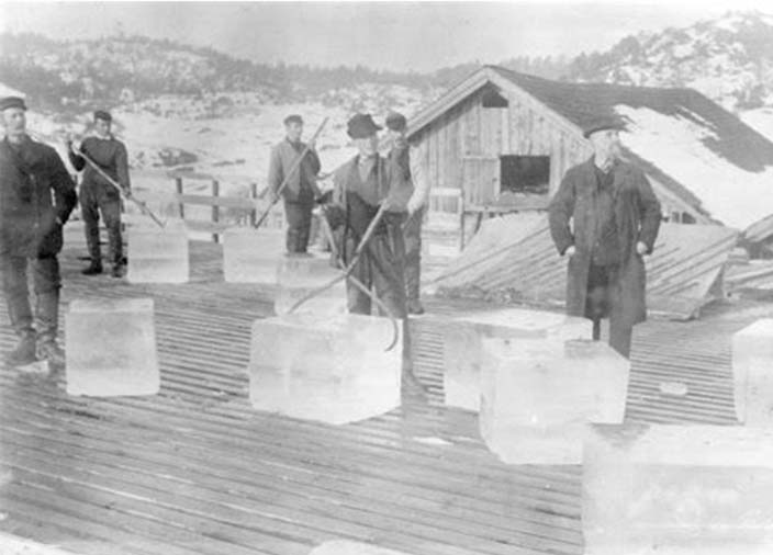Una fotografía antigua en blanco y negro que muestra grandes trozos de hielo de un lago siendo cortados.