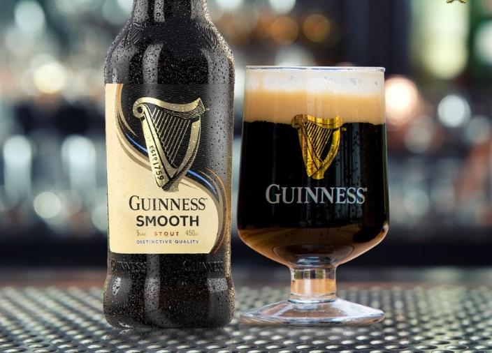 Bottle of Guinness Smooth on table beside glass full of drink