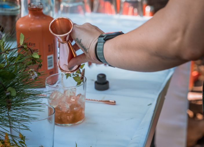 Person_pouring_whiskey_from_measurer_into_glass_of_ice_bourbon_bulleit_bottle_in_background