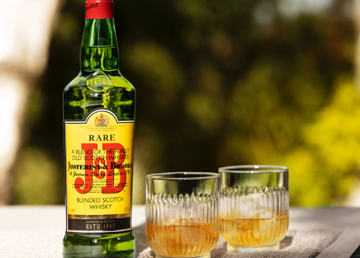 Botella de J&B junto a dos cócteles de whisky en vaso tumbler