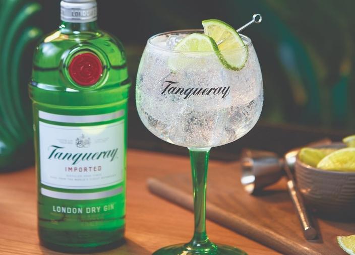 Copa de gin tonic con hielo y lima y una botella de Tanqueray London Dry Gin al fondo