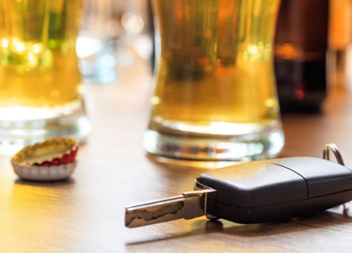 Uma chave de carro em uma mesa de bar com canecas e tampas de garrafa ao fundo.