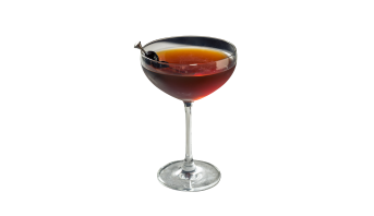 Coquetel de cor âmbar-avermelhado escuro servido em uma taça coupe de vidro transparente. Uma cereja escura espetada em um palito de metal repousa sobre a borda do copo como guarnição. Fundo branco simples.