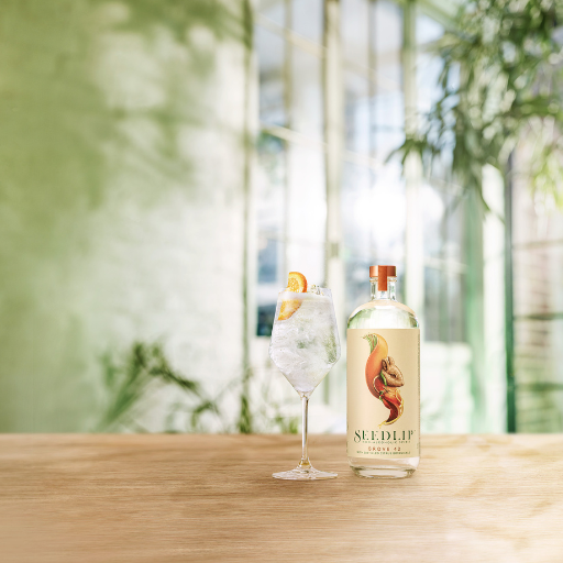 Bottle of Seedlip Grove 42 on table beside cocktail 