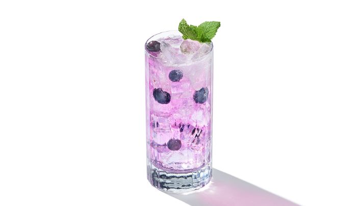 Um coquetel highball roxo em uma mesa redonda de mármore cinza ao lado de um sofá preto