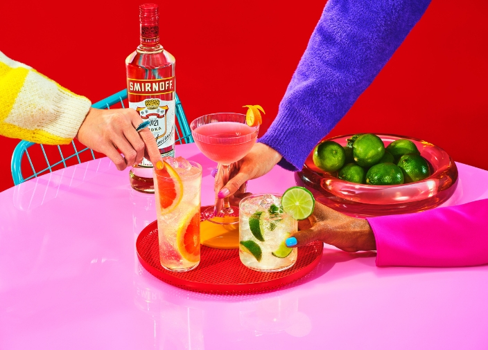 Colourful image of three Smirnoff cocktails on a table with a hand holding each