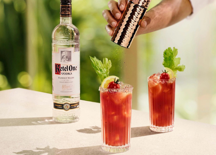 Botella de vodka Ketel One sobre una mesa junto a dos cócteles Bloody Mary.