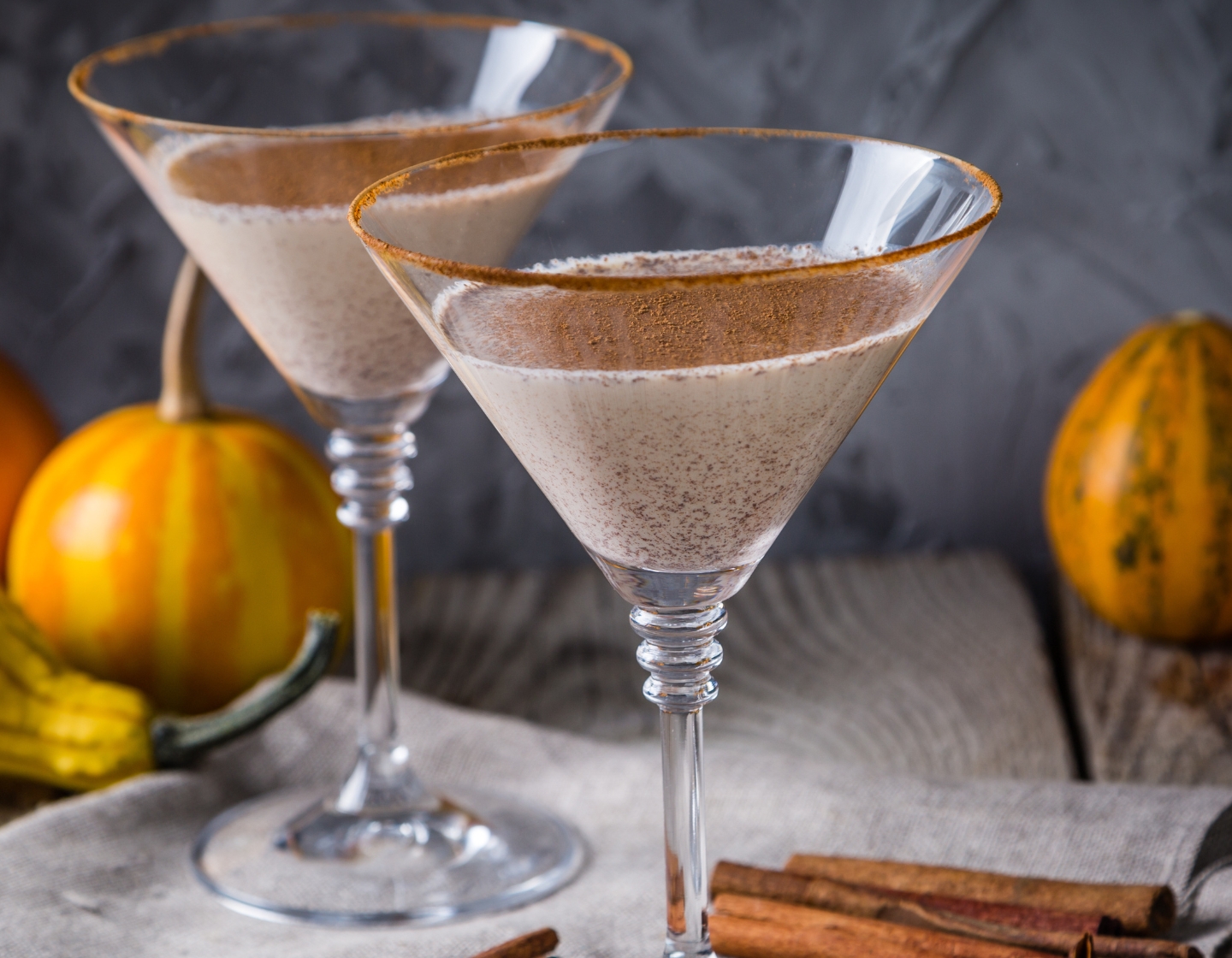Dos vasos de un cóctel Autumn Martini, con ramas de canela y calabazas pequeñas a su alrededor.