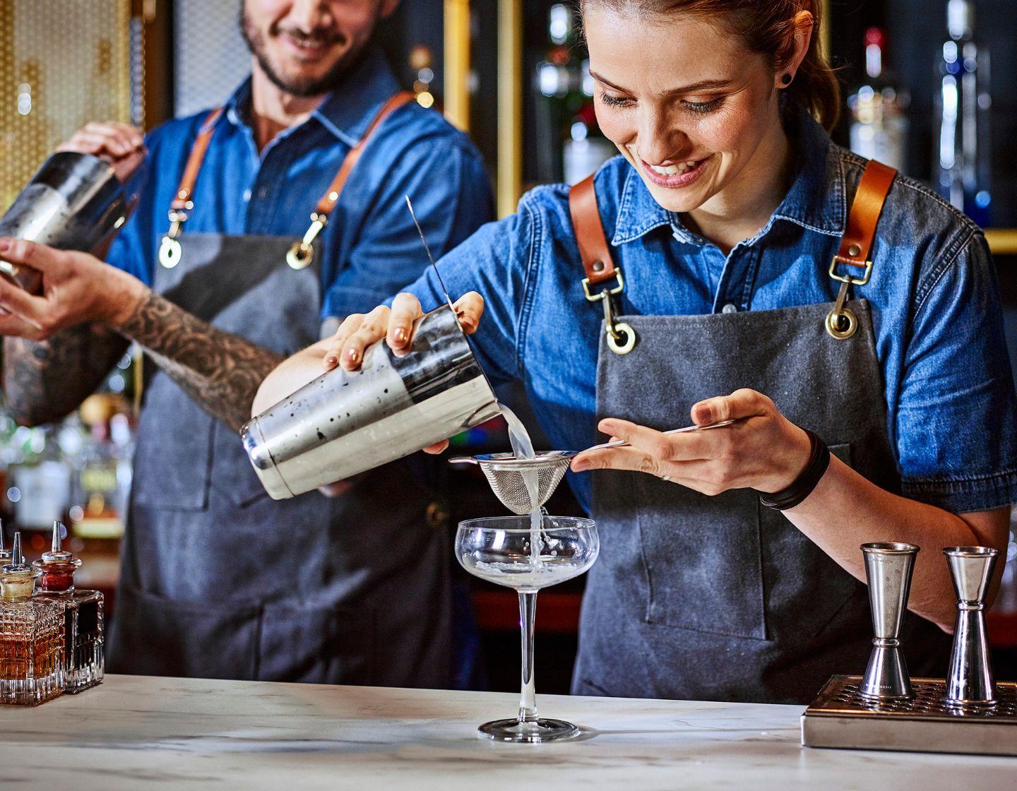 two bartenders behind bar shaking cocktails
