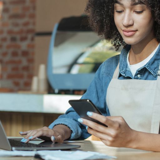 Una mujer con un celular y una laptop usando un delantal de bar
