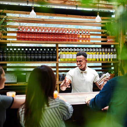Bartender with a cocktail shaker interscting with customers sitting at the bar.