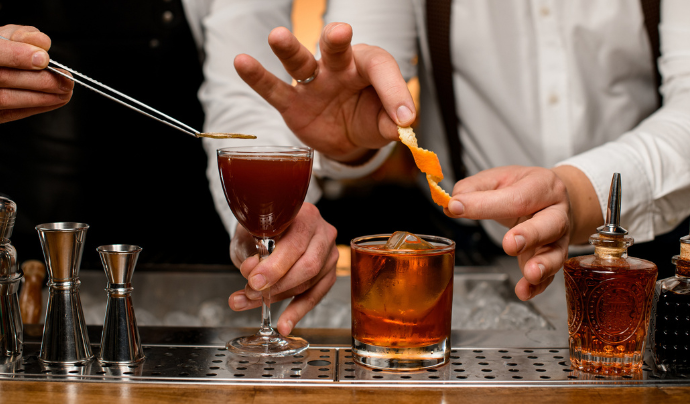 Dos bartenders añaden los toques finales a sus servicios utilizando pinzas para aplicar una garnish de limón.