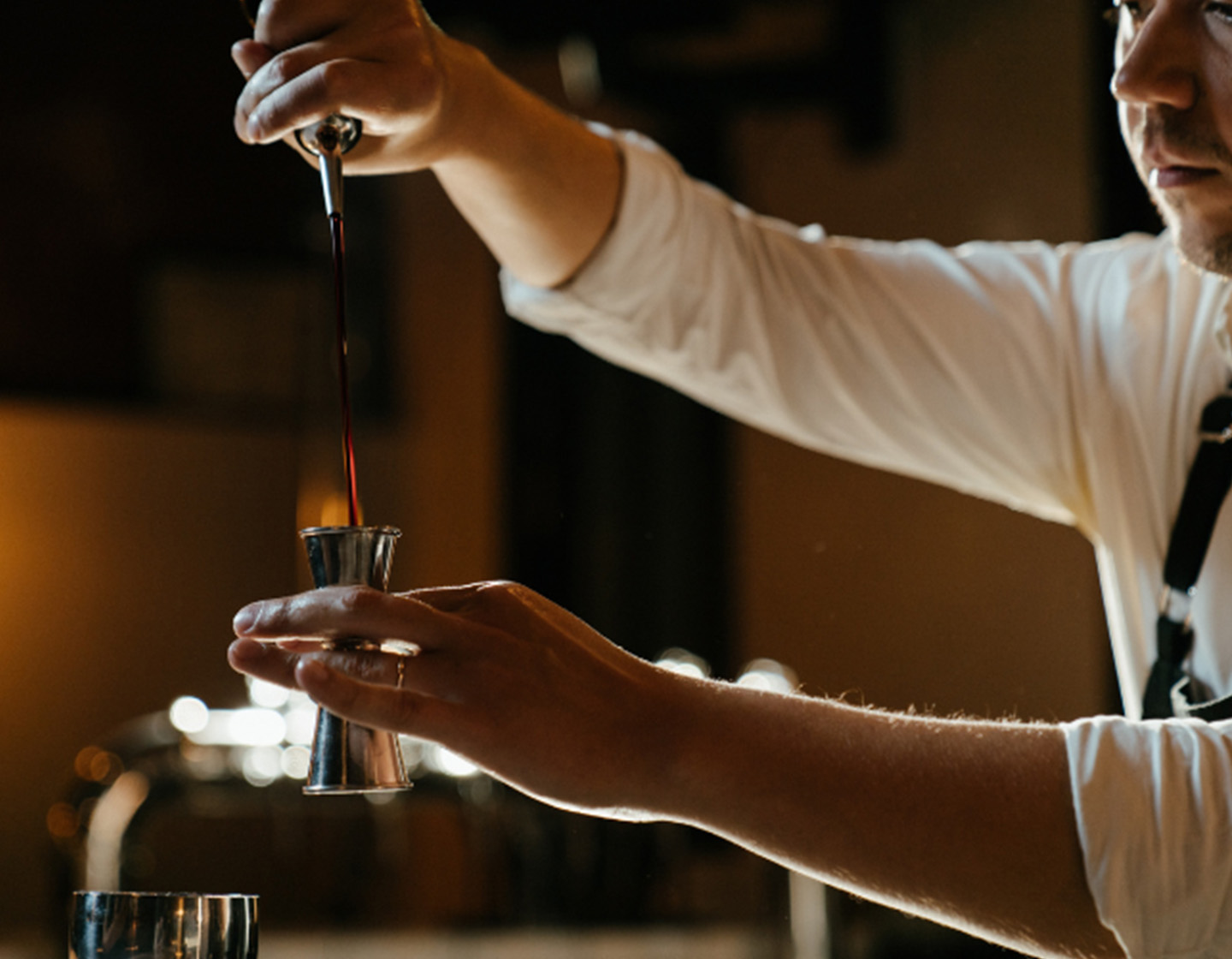 Ein Barkeeper füllt eine Flüssigkeit in einen Jigger. 