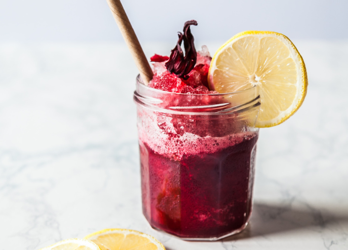 Red cocktail in jam jar with crushed ice and lemon slice