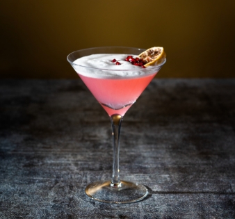 copa martini con licor rosado decorado con garnish de naranja