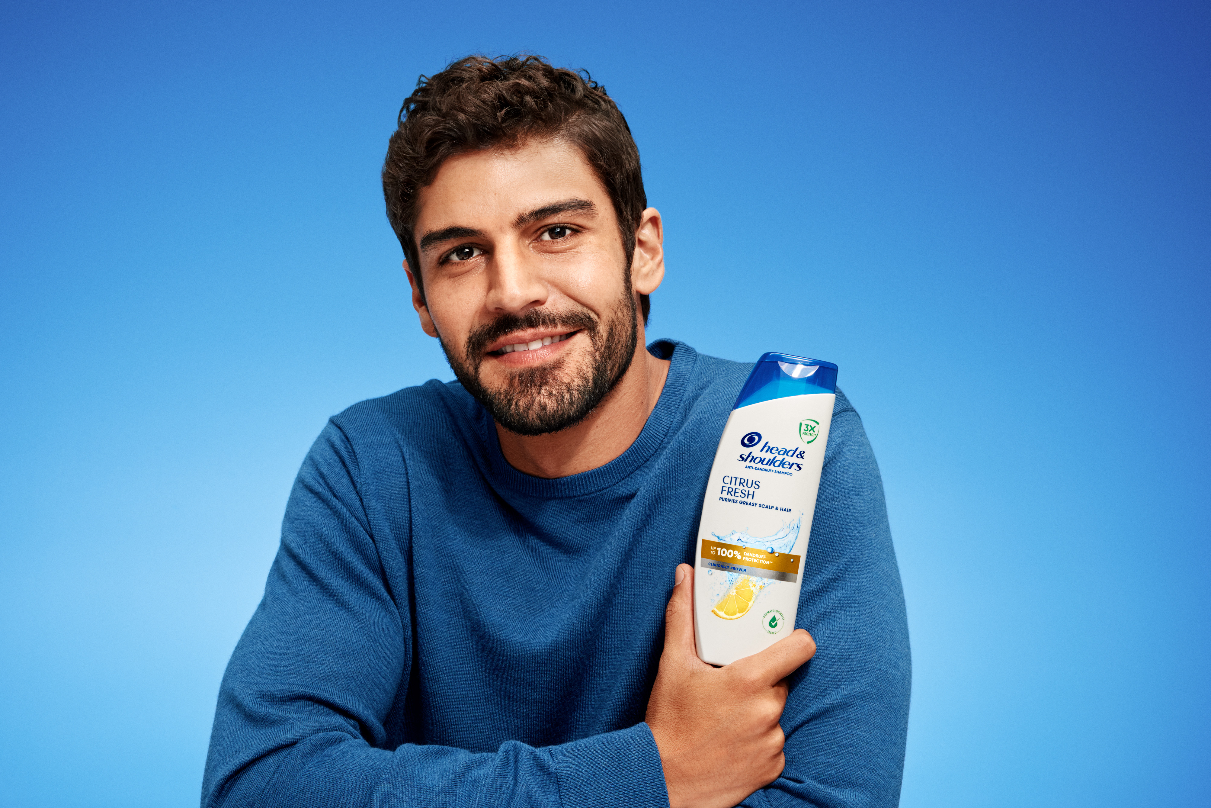 Uomo con barba e shampoo Citrus Fresh, inquadratura ampia su sfondo blu