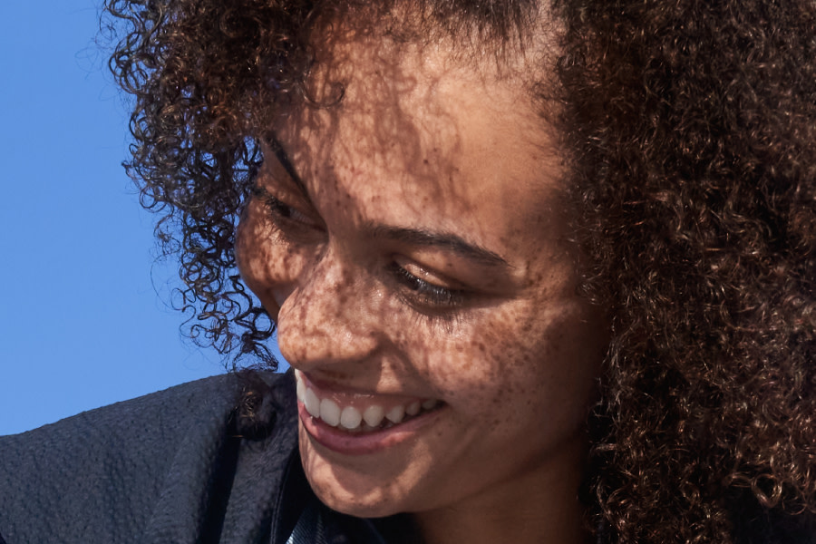 una donna sorridente con i capelli molto ricci guarda di lato
