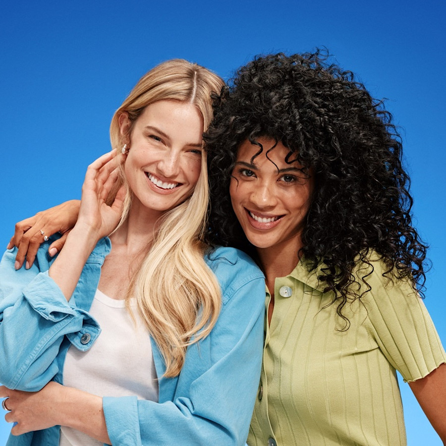 Due amiche sorridenti, una bionda e una riccia, si abbracciano