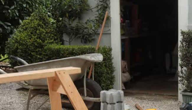 detail of a saw horse and wheelbarrow outside a garden shed